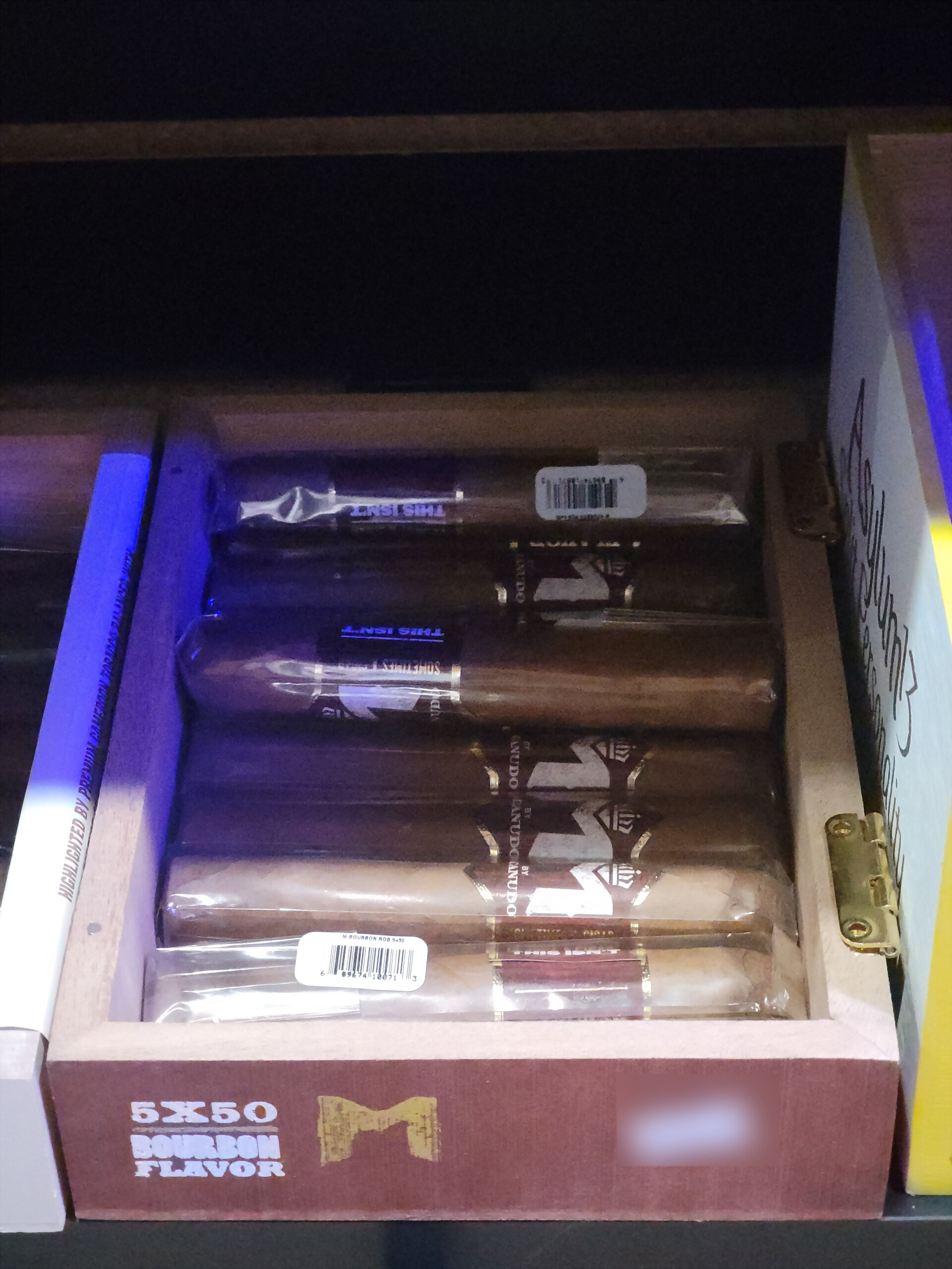 An M by Macanudo Bourbon box open on the shelf, 5X50 BOURBON FLAVOR across the front