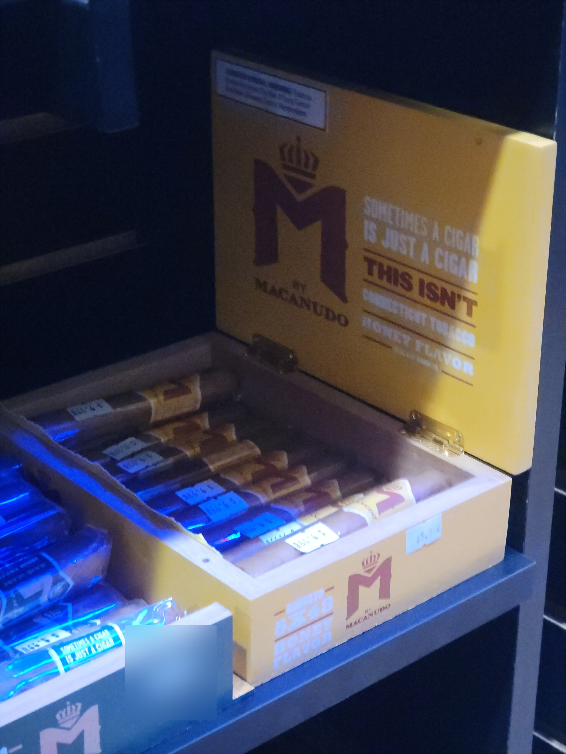 An M by Macanudo Honey box, the yellow lid reading SOMETIMES A CIGAR IS JUST A CIGAR - THIS ISN'T