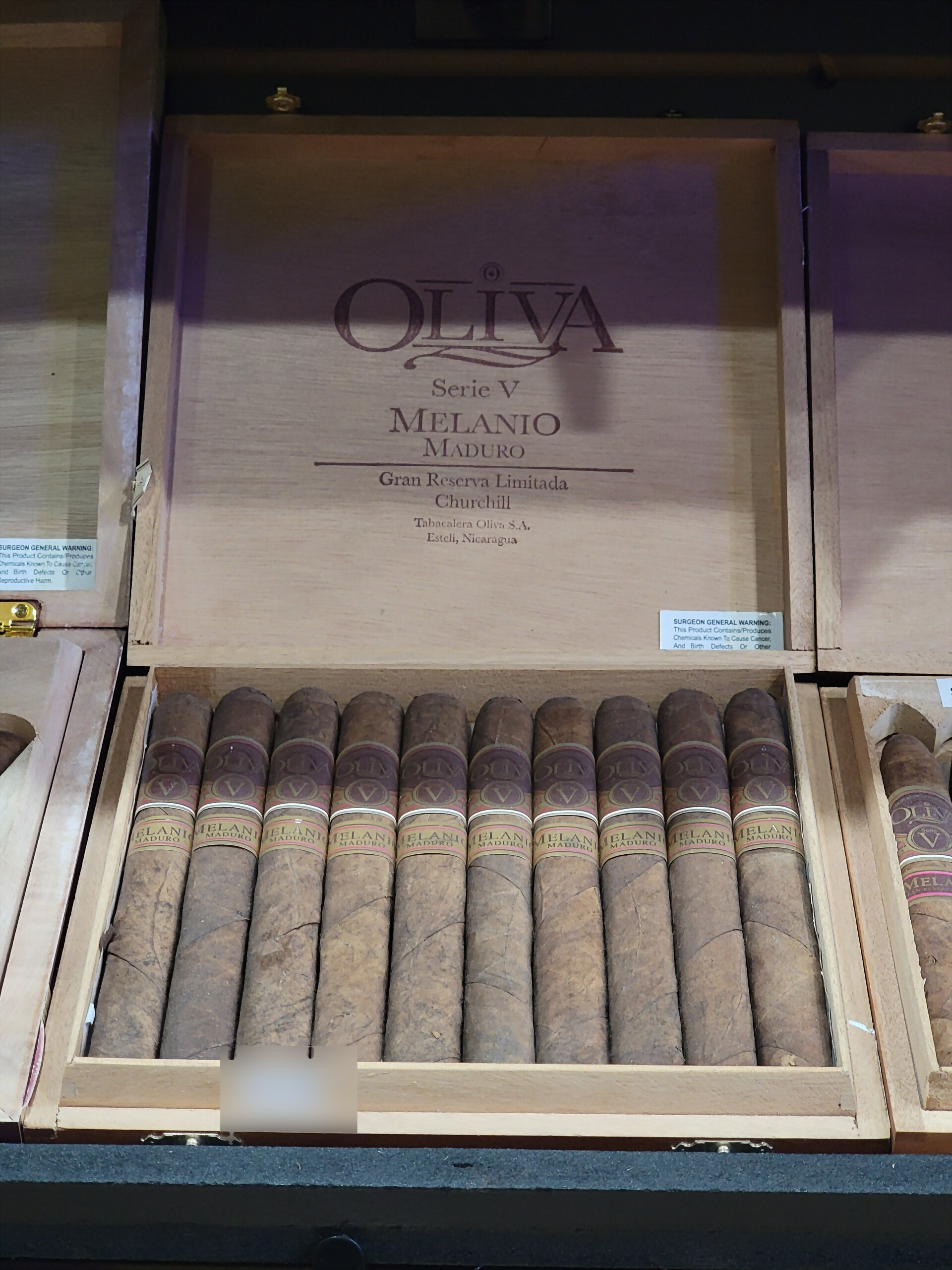 An Oliva Serie V Melanio Maduro Churchill box open on the humidor shelf