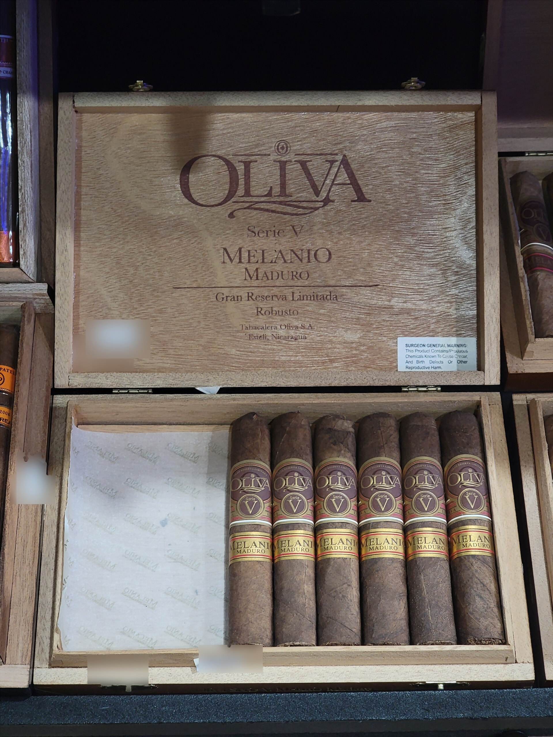 An Oliva Serie V Melanio Maduro Robusto box, lid raised, the Oliva crest burned into the wood