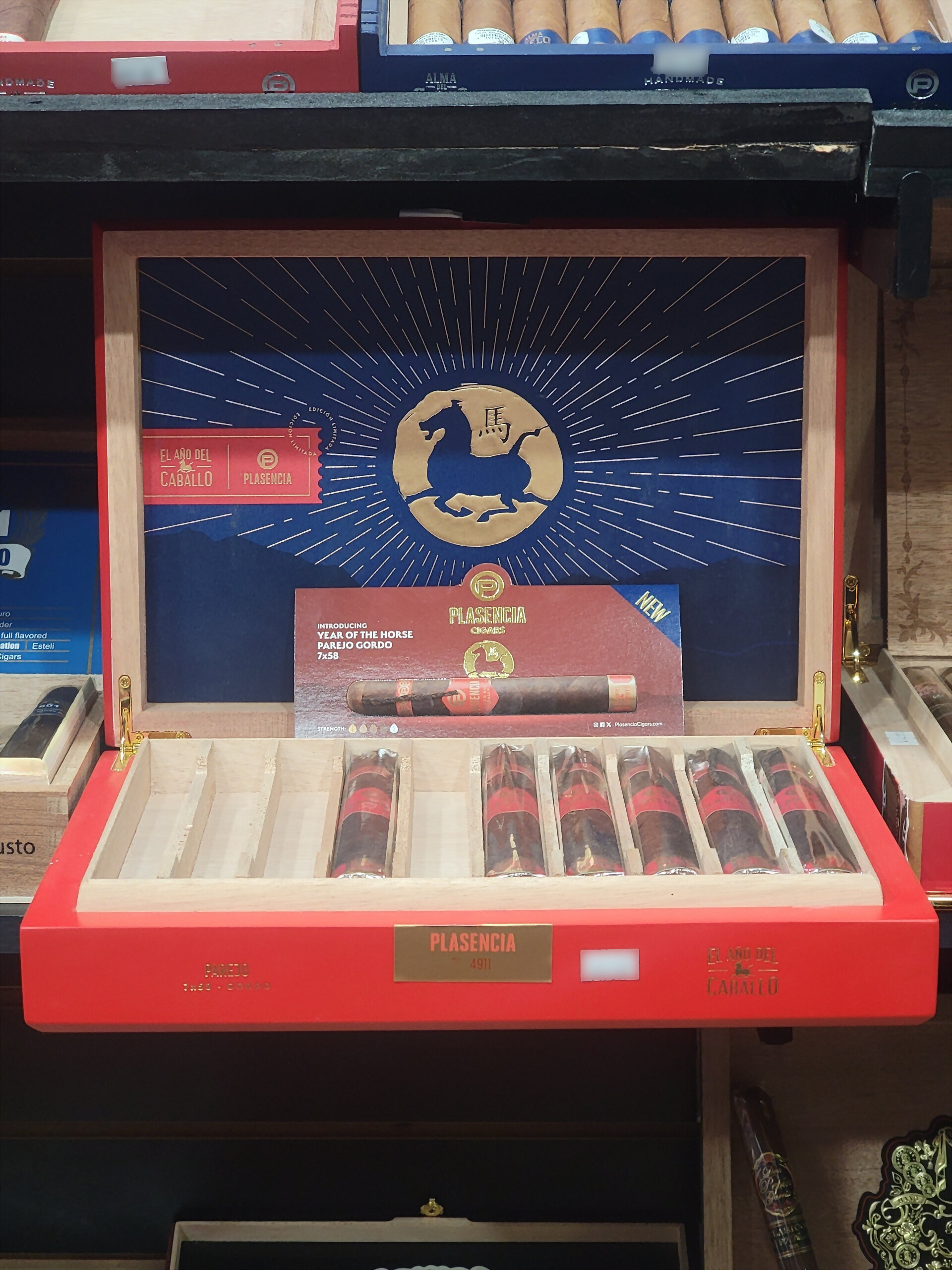 A Plasencia El Año del Caballo box open on the shelf, the gold horse on the blue inner lid above a card reading PAREJO GORDO 7x58