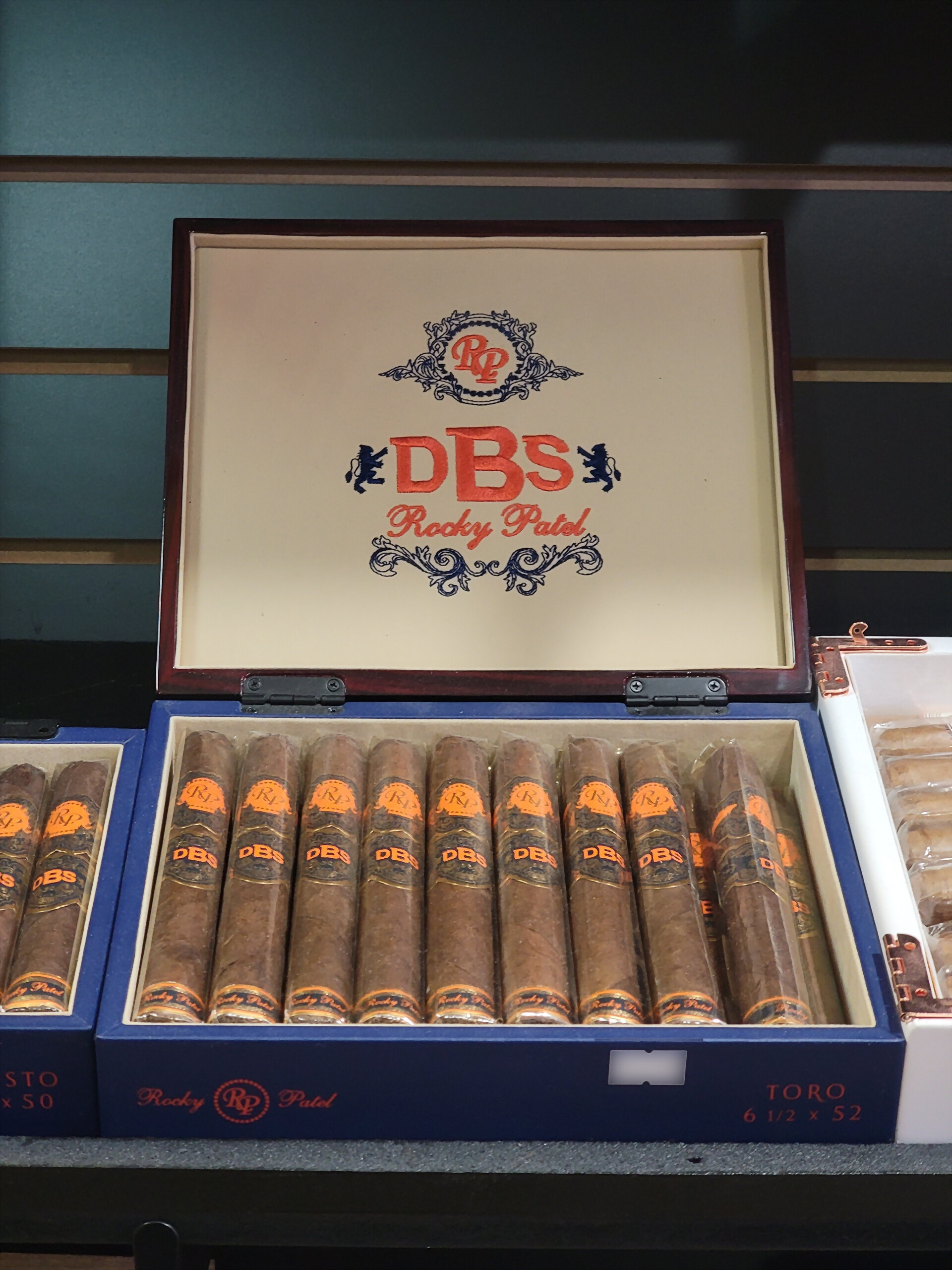 A blue Rocky Patel DBS box open on the shelf, TORO 6 1/2 x 52 on the front rail